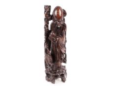 A carved hardwood Chinese figural candle stand in the form of a sage carrying fruit and staff,