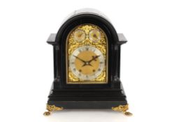 A large 19th Century ebonised mantel clock, the arched case supporting an ornate foliate brass
