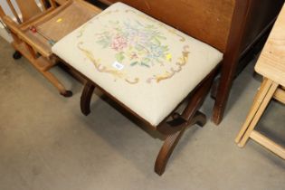 An upholstered stool on cross frame supports