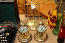 Two anniversary clocks under glass domes and a single glass dome