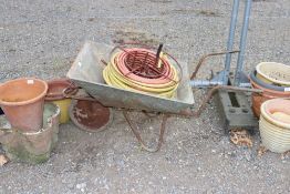 A metal garden wheelbarrow; length of hose on a me
