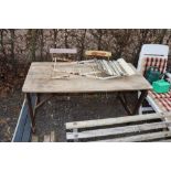 A wooden trestle table and three folding chairs