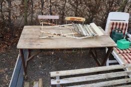 A wooden trestle table and three folding chairs