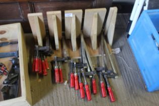 A quantity of assorted clamps mounted to wooden hanging rack