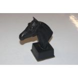 A bronze bust of a horses head raised on square so