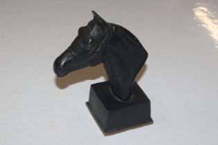 A bronze bust of a horses head raised on square so