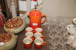 A Le Creuset orange coffee pot and six cups