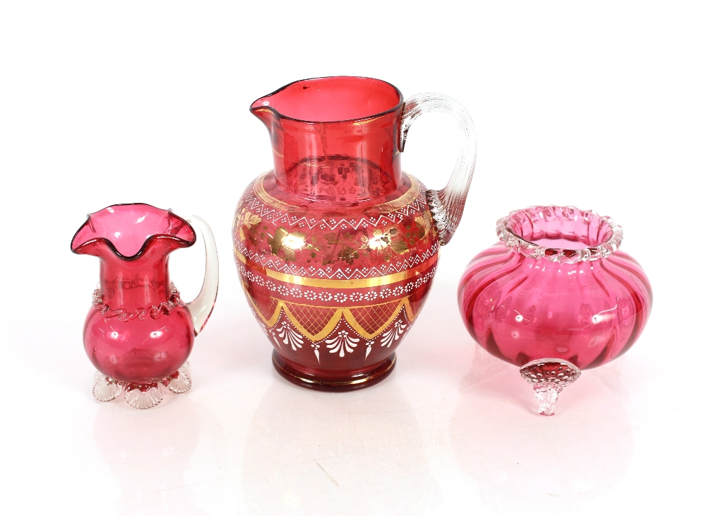 A large cranberry glass jug with enamelled and gilt stylised decoration; a small cranberry glass