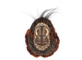An Ethnic face mask with painted seashell and bone decoration to the face, within a wicker and straw