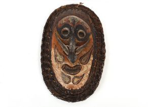 A large oval shield shape Ethnic face mask, having painted decoration and wicker work borders, 60cm