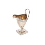 An Edwardian silver pedestal cream jug, having foliate line decoration, spread foot and square base,