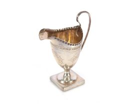 An Edwardian silver pedestal cream jug, having foliate line decoration, spread foot and square base,