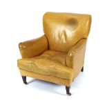 An early 20th Century tan leather covered deep seated armchair, raised on square tapering supports