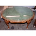 A reproduction mahogany oval coffee table with leather inset top, raised on carved cabriole
