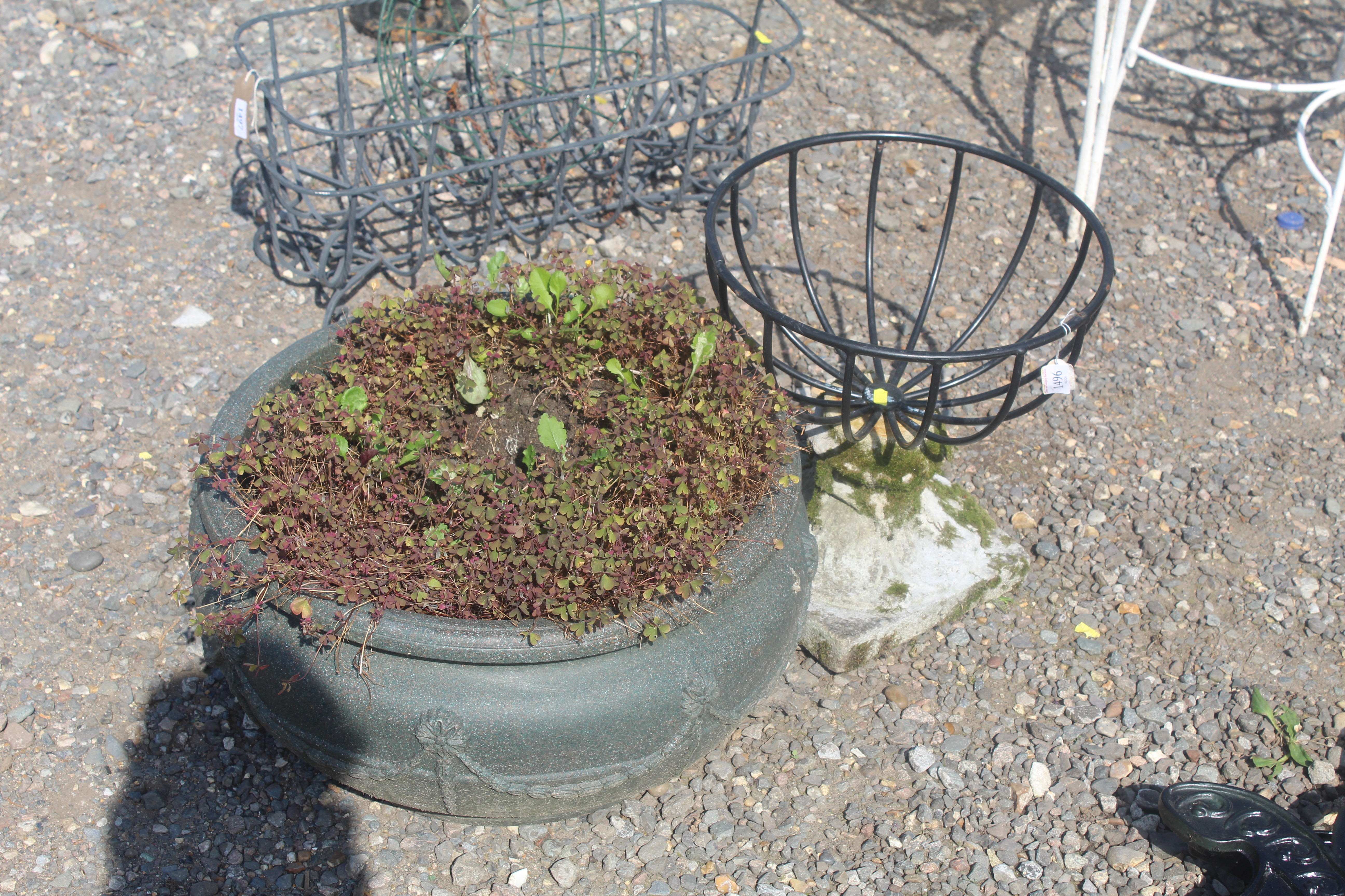 An ornate plastic planter and a metal plant basket attached to a concrete plinth