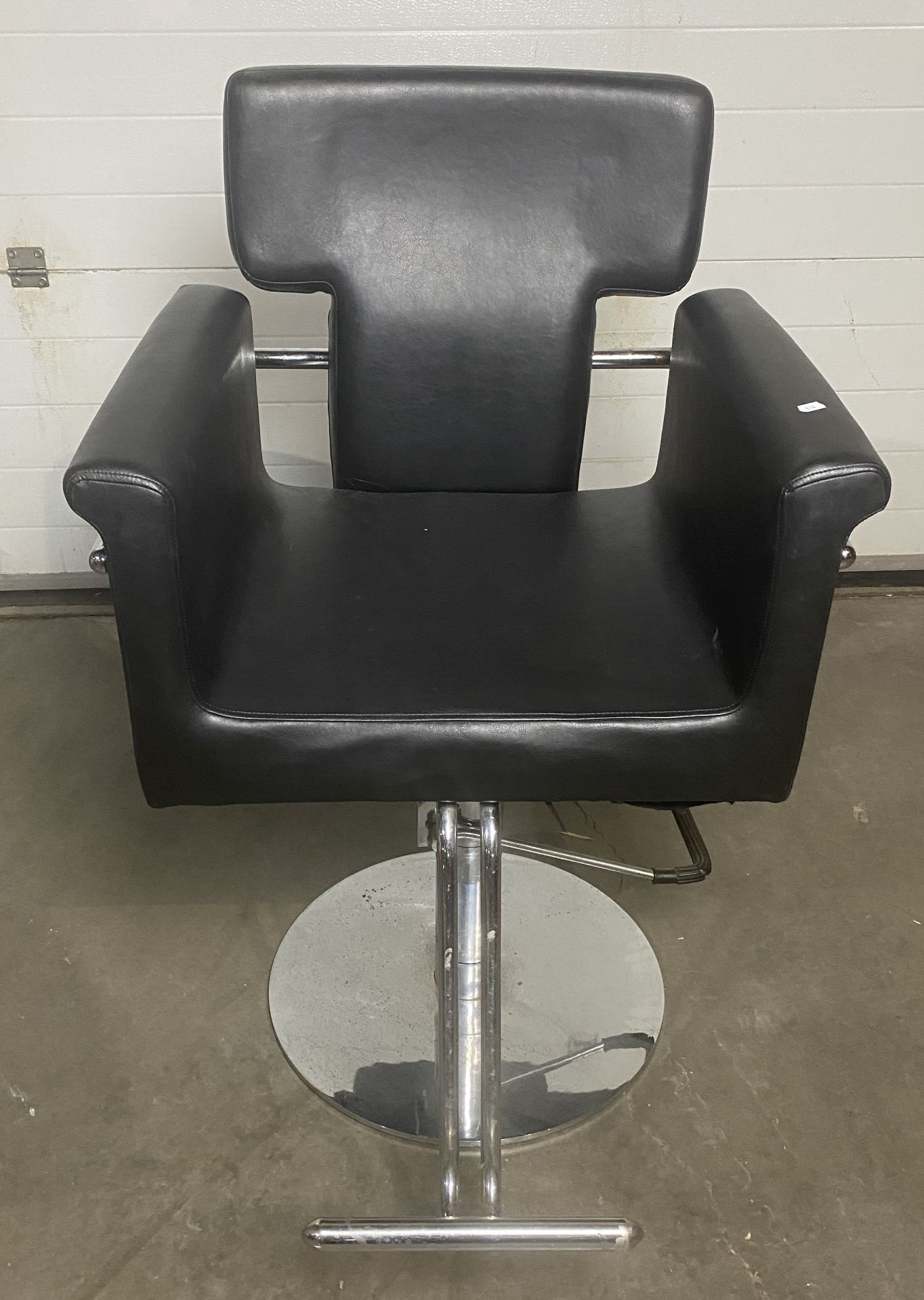 Barbers armchair in black rexine with rounded arms chrome side trail and front-operated pump action,