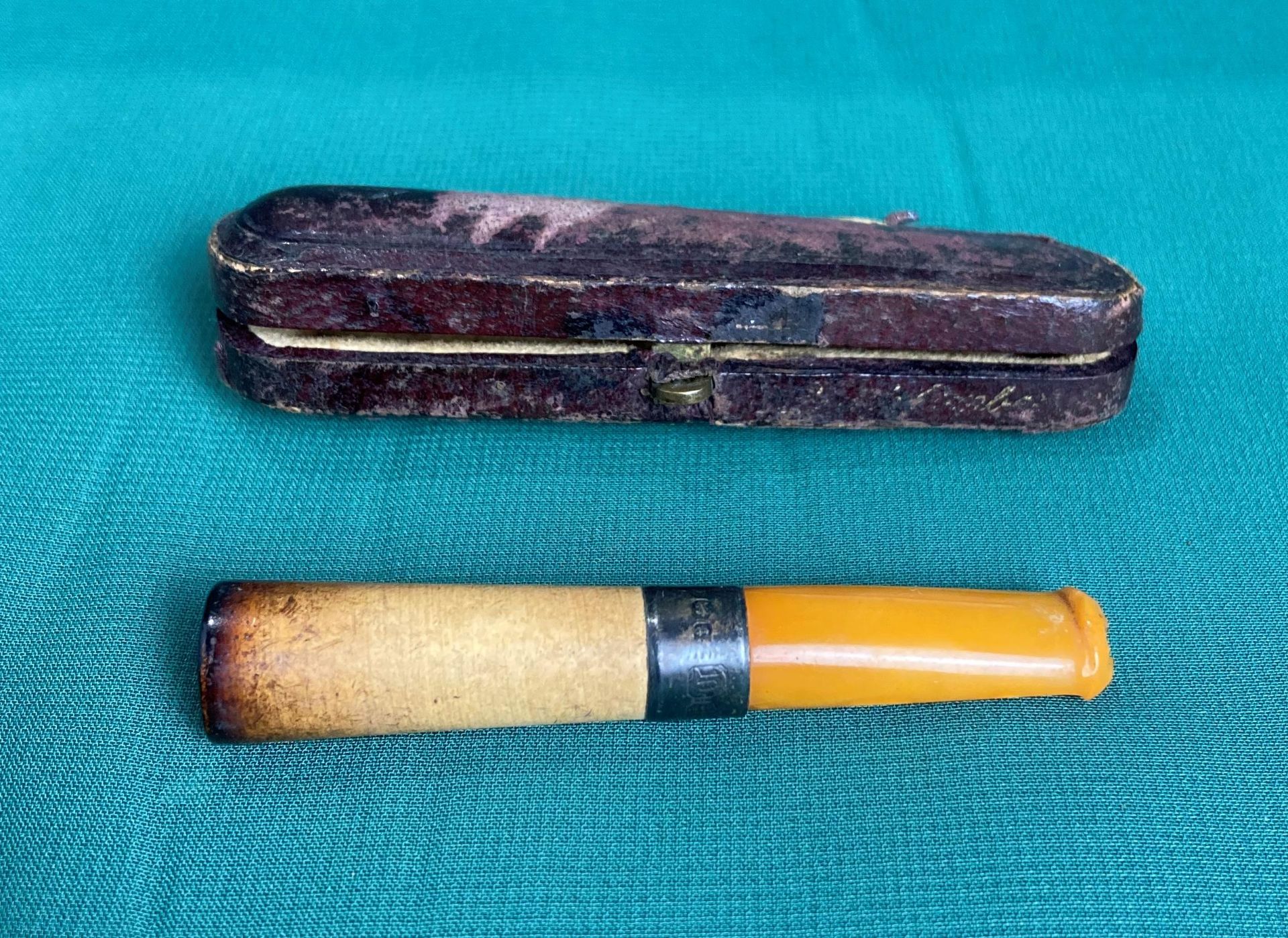 A cigarette holder with possibly amber end and silver collar in original leather case (saleroom