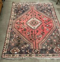 A red, brown and beige patterned Persian style rug with central diamond design,