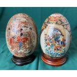 Two Satsuma-style porcelain eggs, both hand painted with Oriental Geisha scenes on wooden bases,
