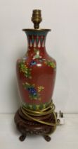 An Oriental cloisonne red lamp with multi-coloured flowers on carved wooden base (no test,