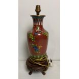 An Oriental cloisonne red lamp with multi-coloured flowers on carved wooden base (no test,