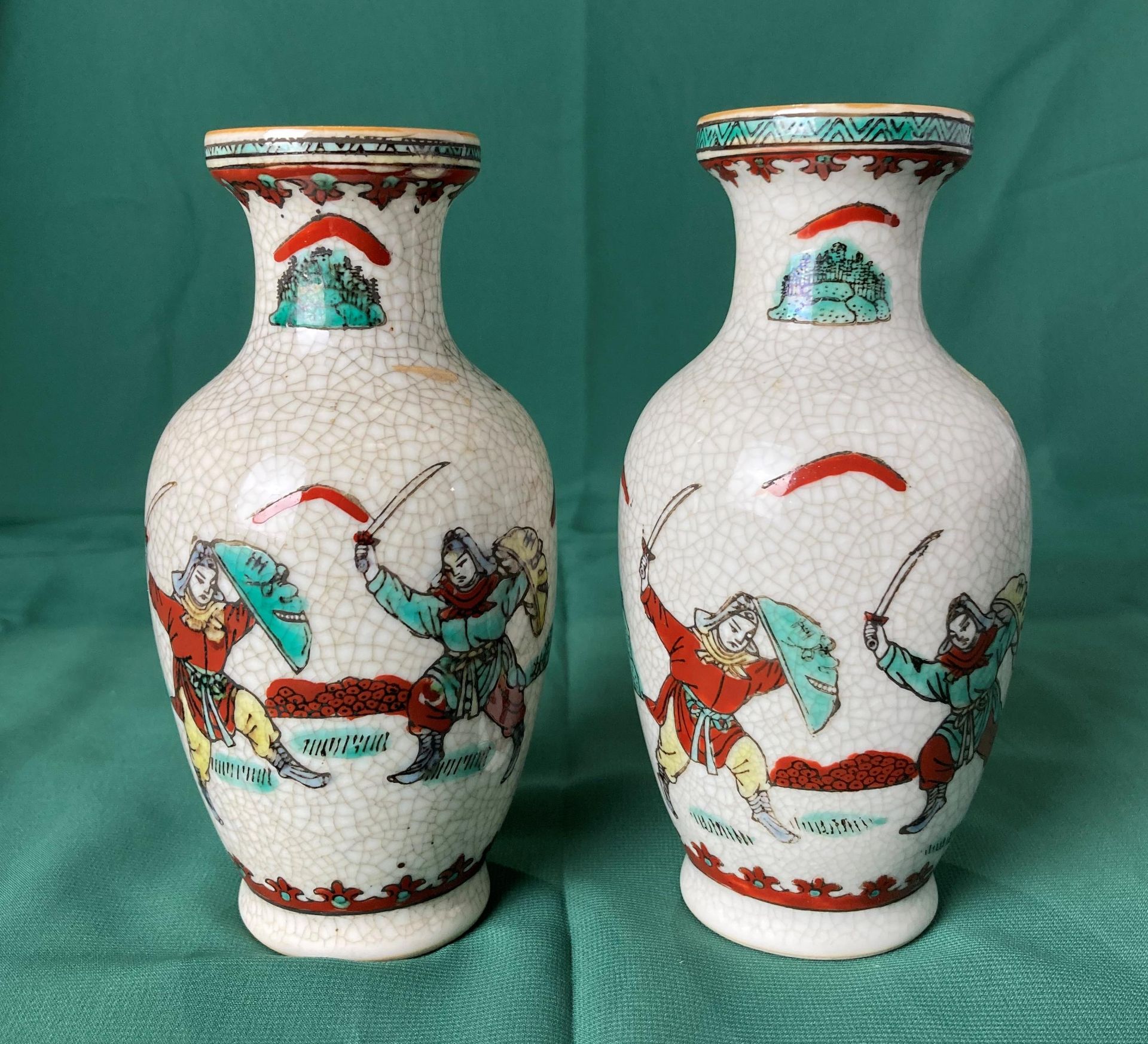 A pair of Oriental vases decorated with fighting warriors in a crackle glaze and stamp to base,