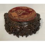 A wooden hand-carved foot stool with carved fruit and foliage vines with red and orange fabric pad