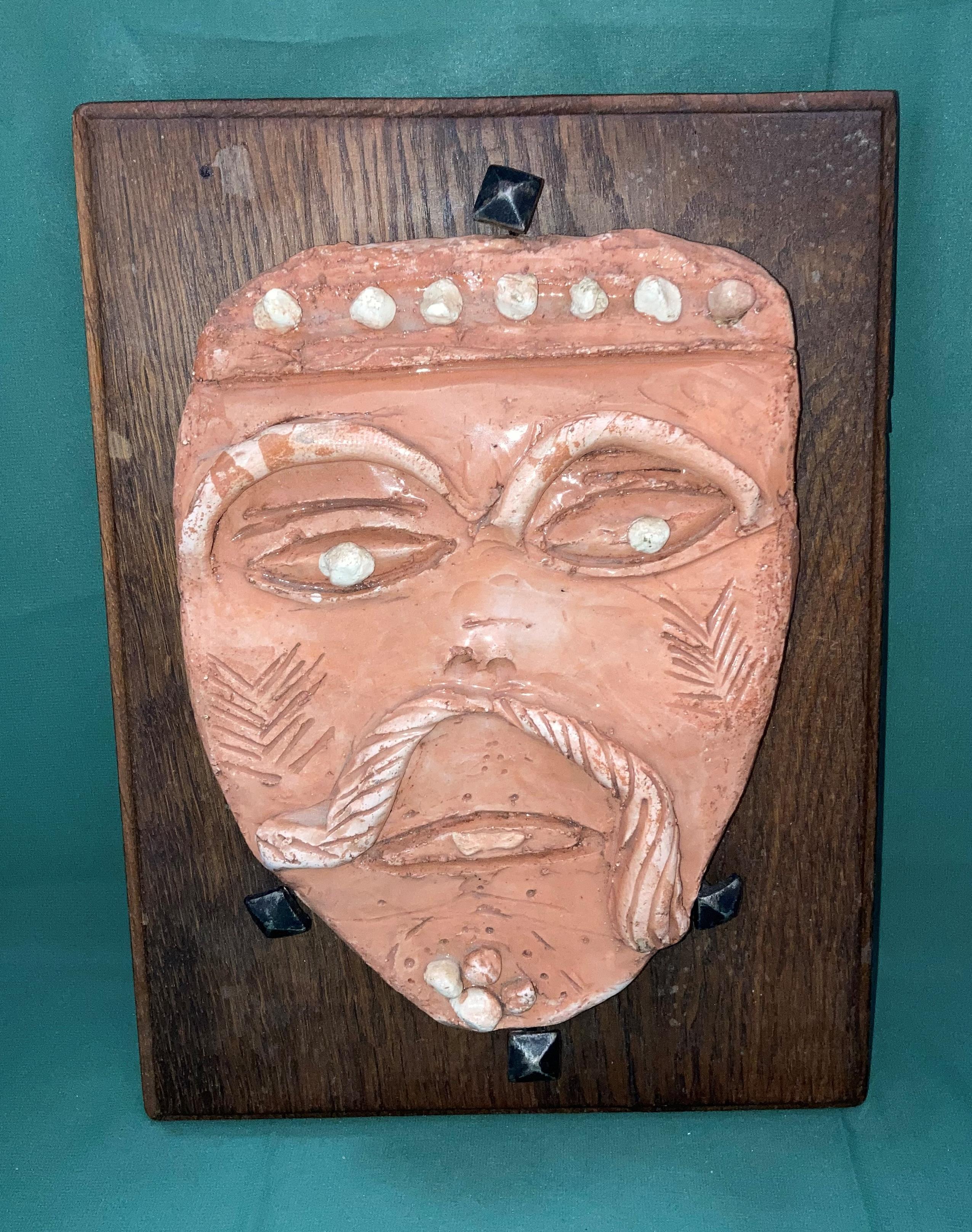 An orange clay glazed mask on oak back with vintage square end nails (mask possibly French) with