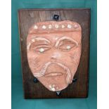 An orange clay glazed mask on oak back with vintage square end nails (mask possibly French) with