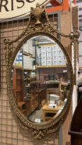 An oval gilt framed mirror with urn to top,