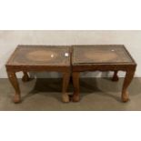 A pair of Asian hand-carved wooden tables with glass tops and with a floral design to each table,