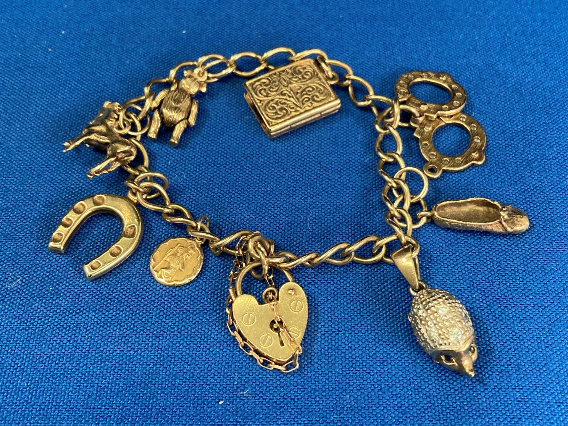 9ct gold charm gate bracelet with heart-shaped clasp and charms, 7" long.