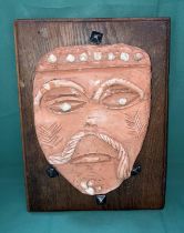 An orange clay glazed mask on oak back with vintage square end nails (mask possibly French) with