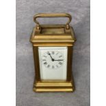A vintage brass miniature carriage clock with white enamel face and Roman numerals,