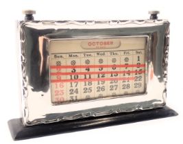 A George V silver cased and ebonised desk calendar, the silvered frame with waved border, in a black