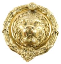 A large brass lion mask door knocker, with circular wreath decorated with flower heads, ribbons, etc