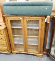 A pine two door glass display cabinet and a green footstool.