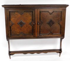 An early 20thC oak wall hanging cupboard, the outswept pediment over a pair of panelled doors enclos