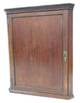 A George III mahogany hanging corner cupboard, with moulded cornice, single panelled door with brass