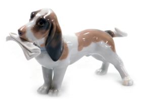 A Lladro figure of a Bassett hound, with newspaper to the mouth, printed marks beneath, 19cm wide.