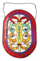 A 20thC stained leaded glass panel, of oval form, decorated centrally with a scrolling motif surroun