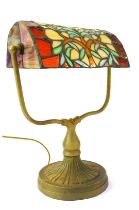 A Tiffany style desk lamp, the leaded glass shade decorated with a tree raised on a cast metal base