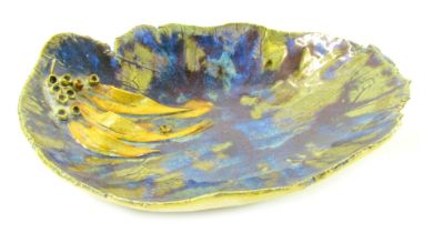 A studio pottery dish, of abstract form, in blue oxide glaze with applied leaf and berry decoration,