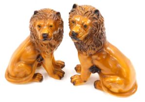 A pair of early 20thC chalkware models of seated lions, each painted in shades of brown, 33cm high.