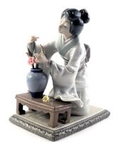 A Lladro porcelain figure of an oriental lady with a vase of flowers, 20cm high, boxed. (AF)