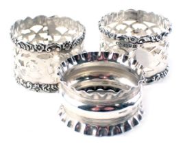 Three silver napkin rings, comprising a pair of pierced and floral design, and one with fluted borde