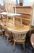 A pine oval kitchen table, three slatted chairs, and a wall rack with three shelves.