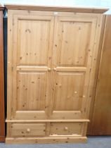 A pine two door wardrobe, with two drawers on block base.