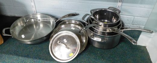 A group of stainless steel Le Crueset saucepans and lids, and a frying pan.