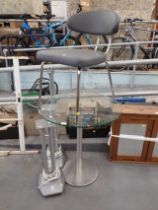 A circular glass table, silver bar stool and two speaker stands.